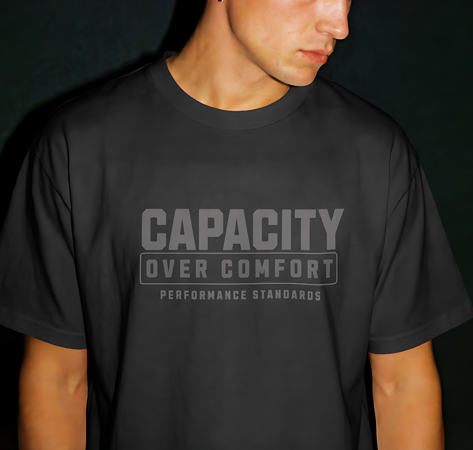 Person wearing a black t-shirt with 'Capacity Over Comfort' text on a dark background